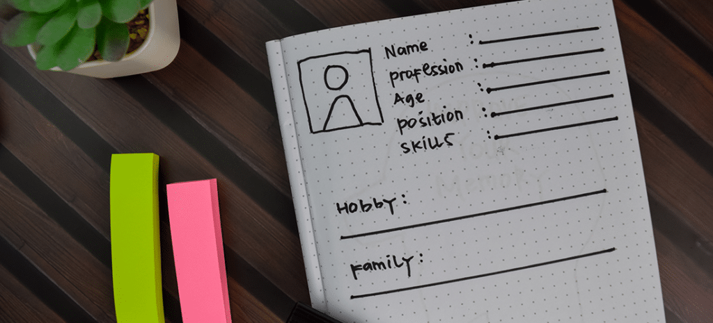 A designer sketches out a the specifics of a user persona at a wooden desk.