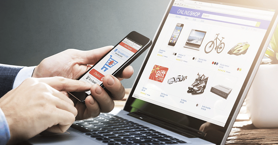 a hand navigates a mobile eCommerce site in front of a laptop