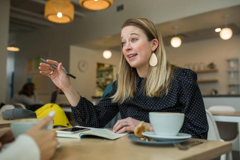 a woman talks across a table to another person while gesturing with her right hand