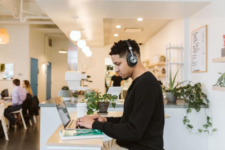 a man wears headphones while working on a laptop in a small coffee shop